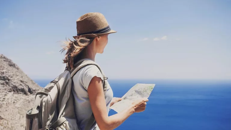 Young girl holding map and looking at the sea, active lifestyle, hiking and travel concept